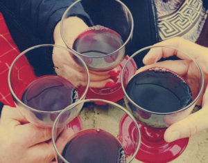 cztery osoby trzymają w dłoniach kieliszki w których znajduje się wino. Stukaja się nimi składając sobie życzenia